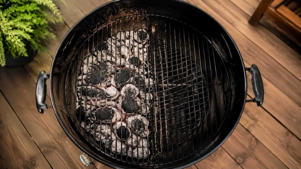 Overhead view of a charcoal kettle grill set up with a two-zone fire, coals banked on one side and empty grate on the other